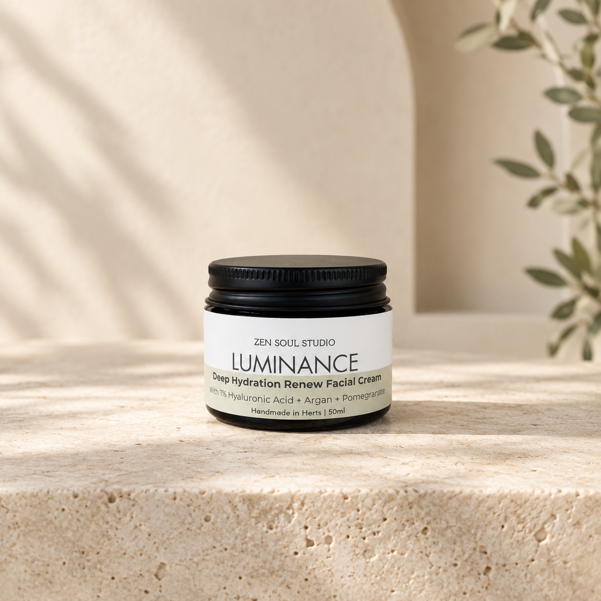Zen Soul Studio LUMINANCE Deep Hydration Renew Facial Cream sits on a textured beige stone surface with soft shadow overlays and a blurred plant in the background.